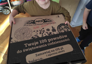 Chłopiec niesie pudełko z pizzą.