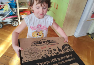 Dziewczynka niesie pudełko z pizzą.