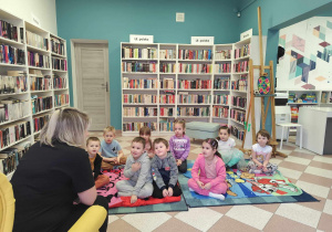 Dzieci słuchają czytanej przez bibliotekarkę bajki.