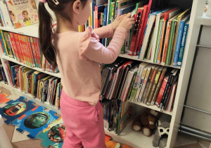 Dziewczynka przegląda regał z książkami dla dzieci.